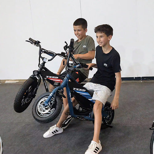 Two young visitors sitting on TXED electric bikes at an exhibition.