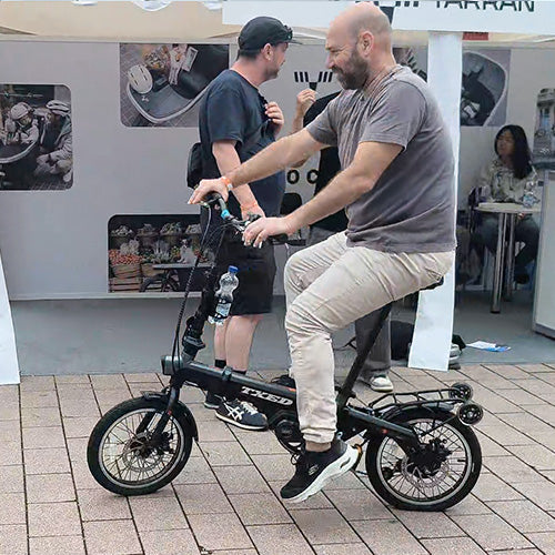 Visitor test riding a compact TXED electric bike at an outdoor exhibition.