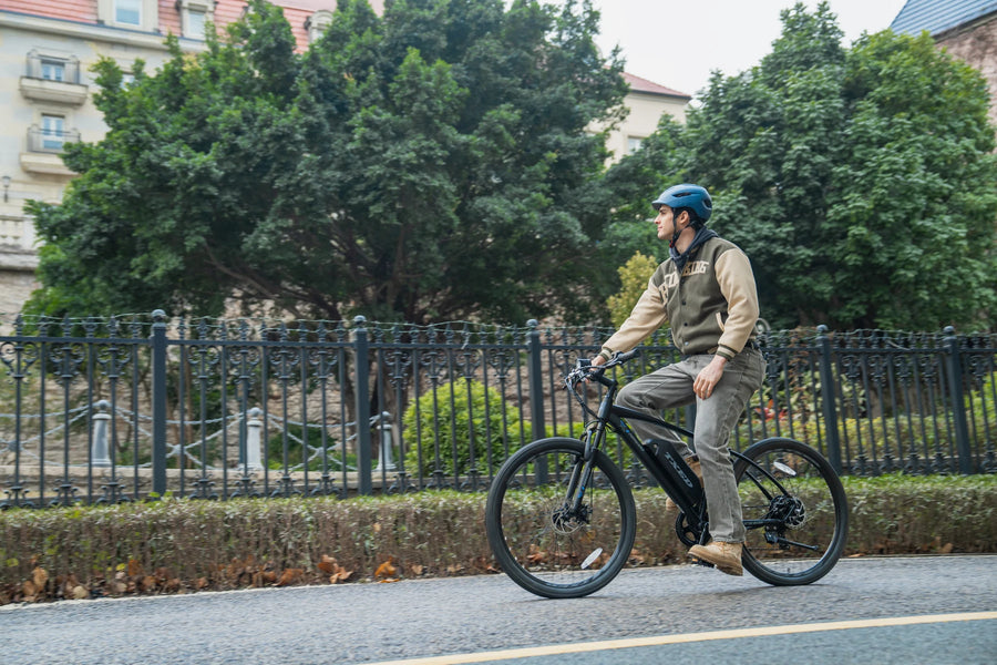 A helmeted rider on a TXED Trail on a paved street beside trees and railings.